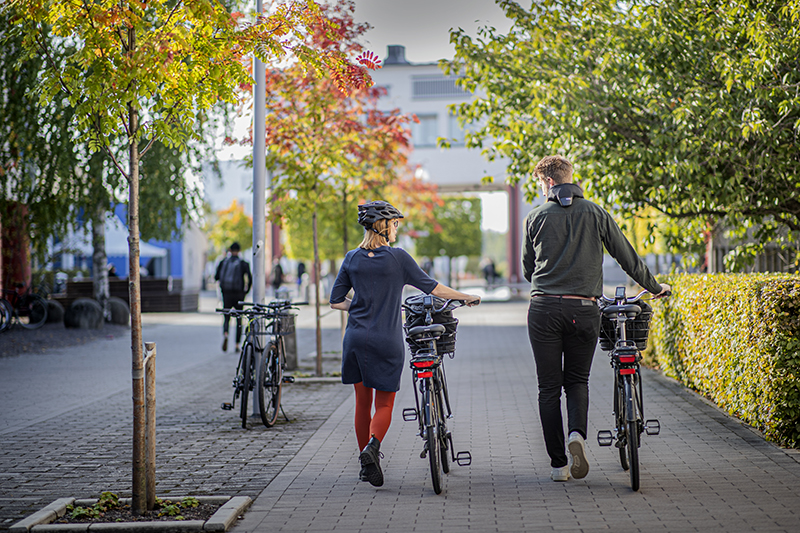 Två personer leder cyklar på campus Örebro