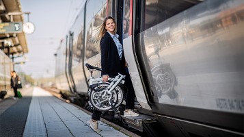 En kvinna går på ett tåg med en vikcykel i handen