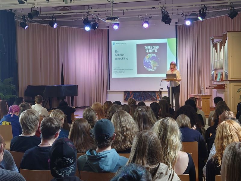 En kvinna föreläser för ett stort antal åhörare. Hon står på en scen och i bakgrunden ser man en presentation med texten "En hållbar utveckling"