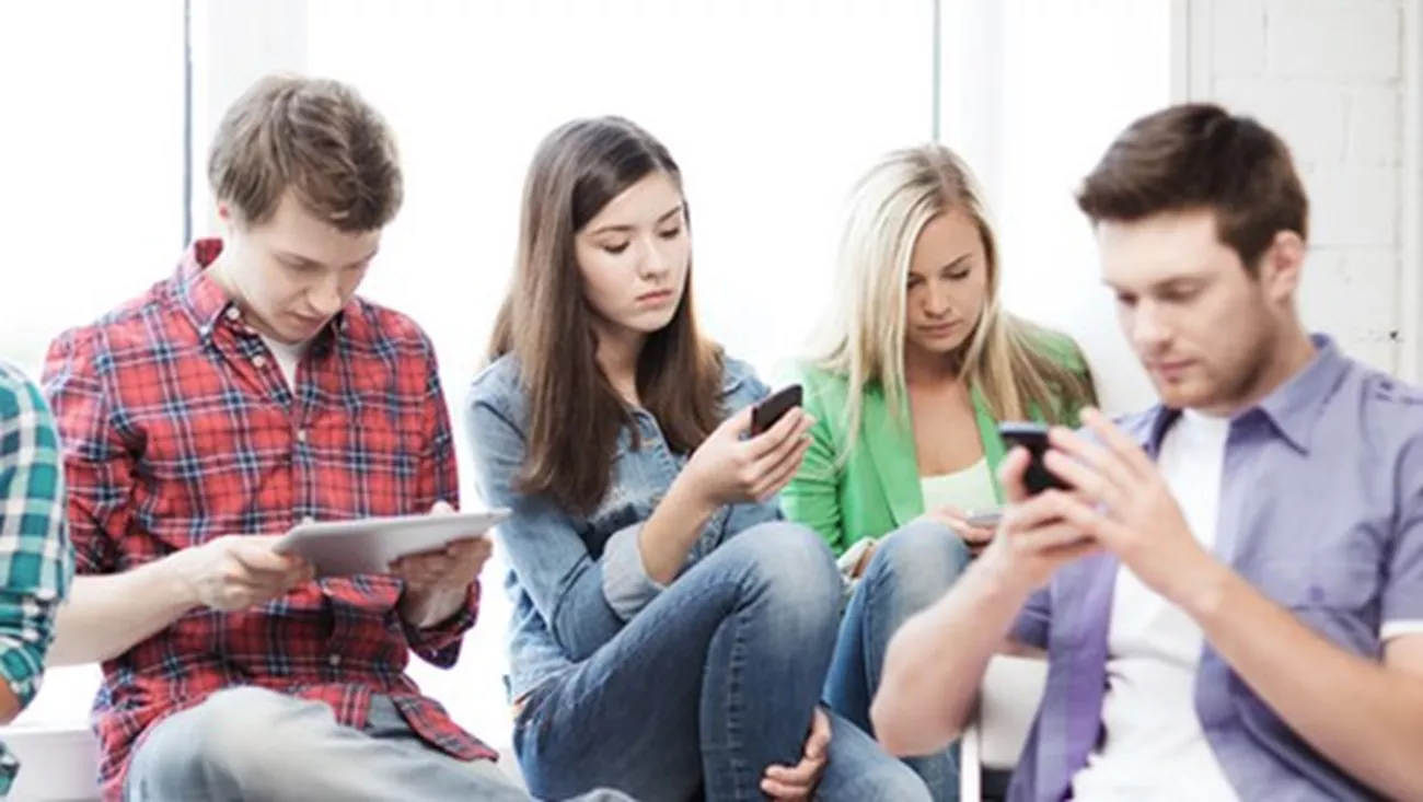 En grupp ungdomar sitter med läsplattor och mobiler.
