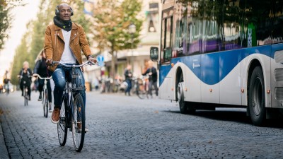 Cyklande person på kullerstensgata. En buss kör förbi i motsatt riktning