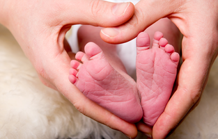 Händer bildar ett hjärta runt en bebis fötter.