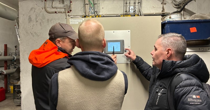 Tre personer framför en elcentral med display