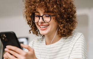 Smiling young woman on the phone in the kitchen, sitting with earphones
