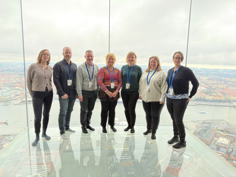 Gruppbild på sju personer i en balkong av glas. En storstad utanför.