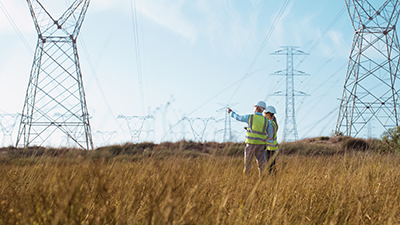 Ett fält med kraftledningar. Två personer i varselkläder.