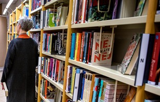 Person står vid  en bokhylla på ett bibliotek