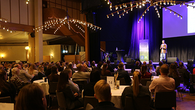 Konferens. En person på scen, åhörare i förgrunden