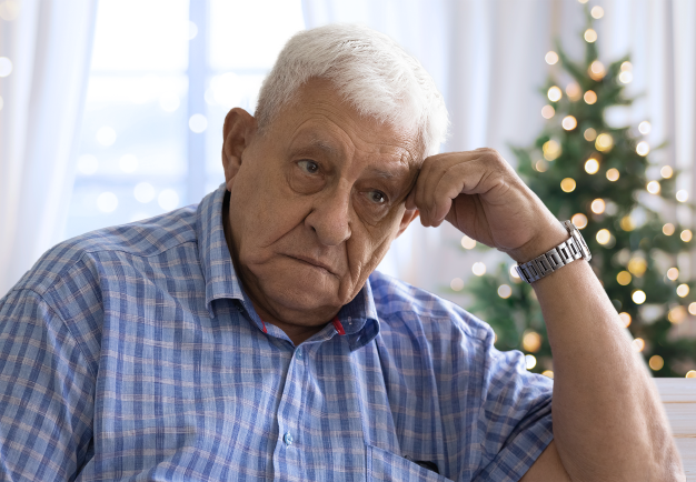 Äldre man ser bekymrad och ledsen ut. I bakgrunden en julgran.