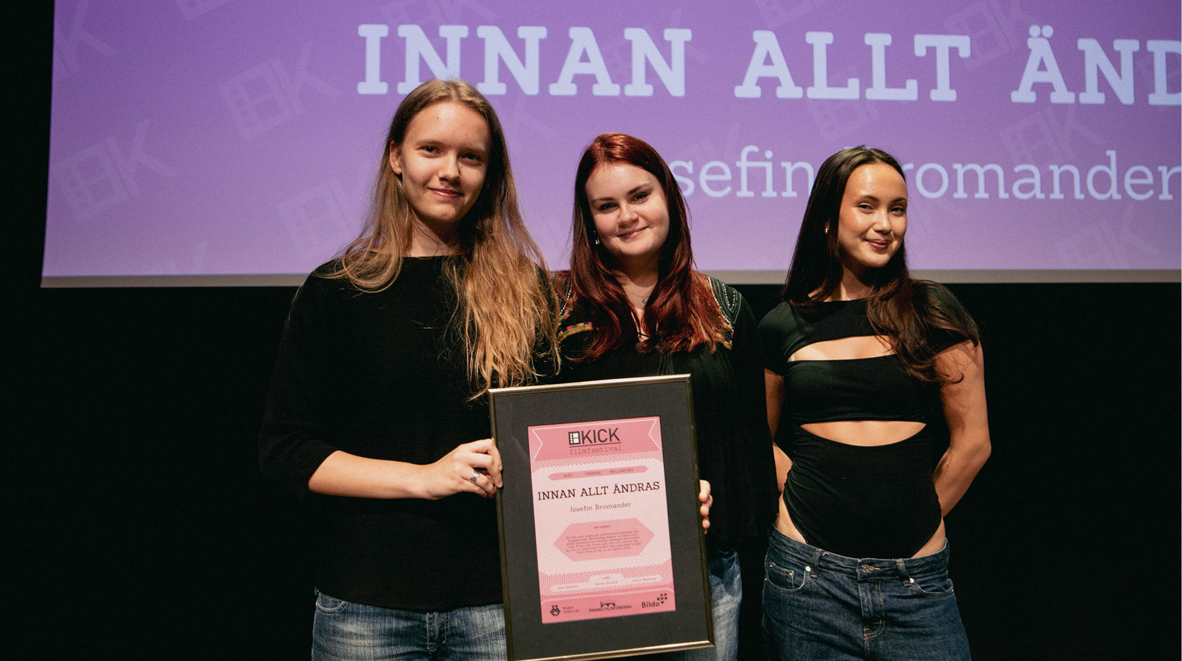 Tre unga tjejer på scen, en håller i ett diplom