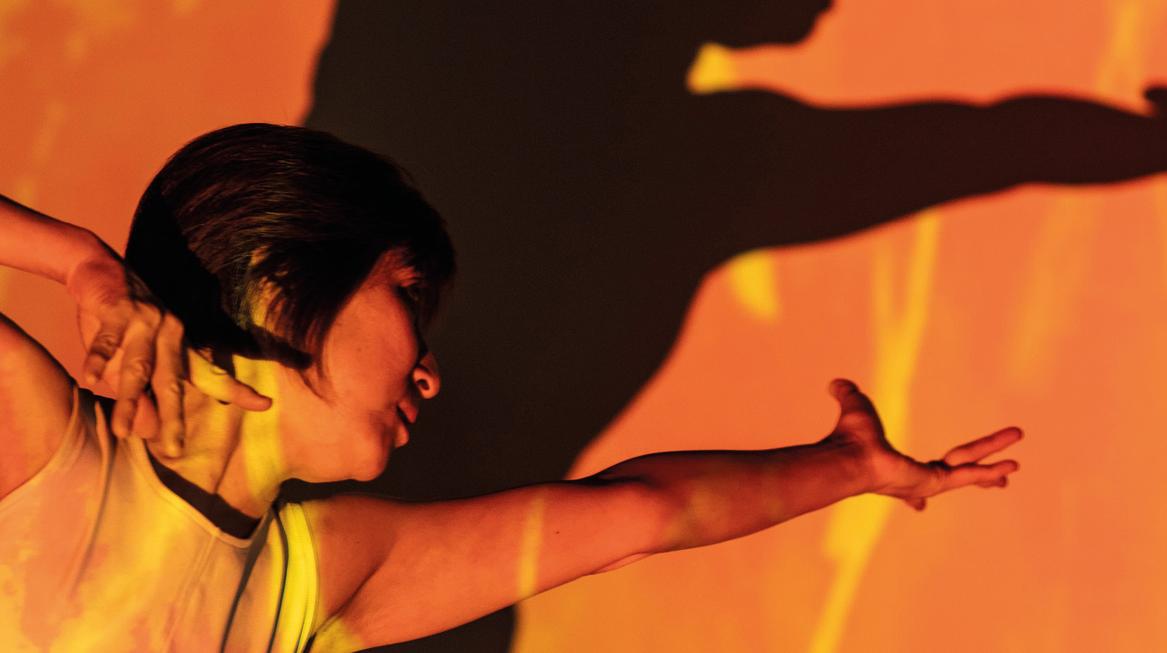 Dansare med dramatisk mörk skugga mot orange bakgrund