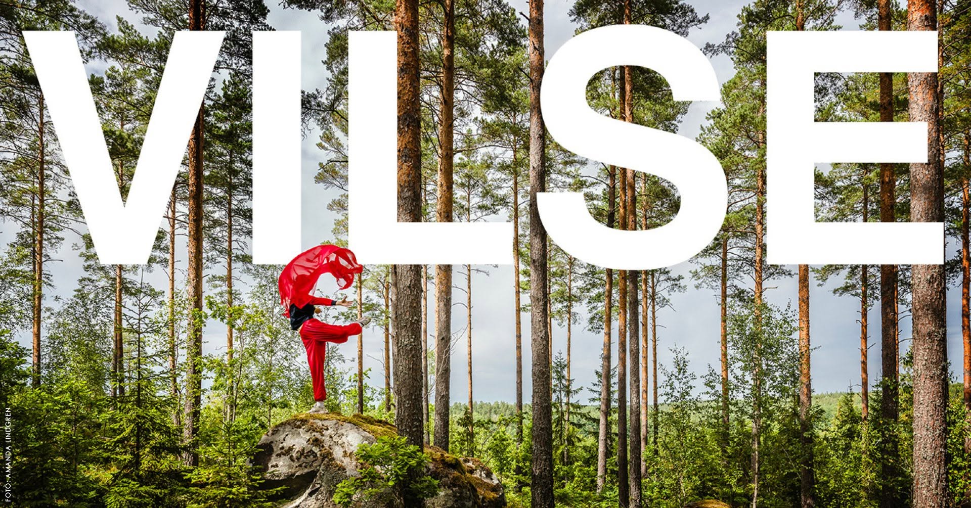 Dansare med röd sjal och röda byxor på en sten i grönskande skog
