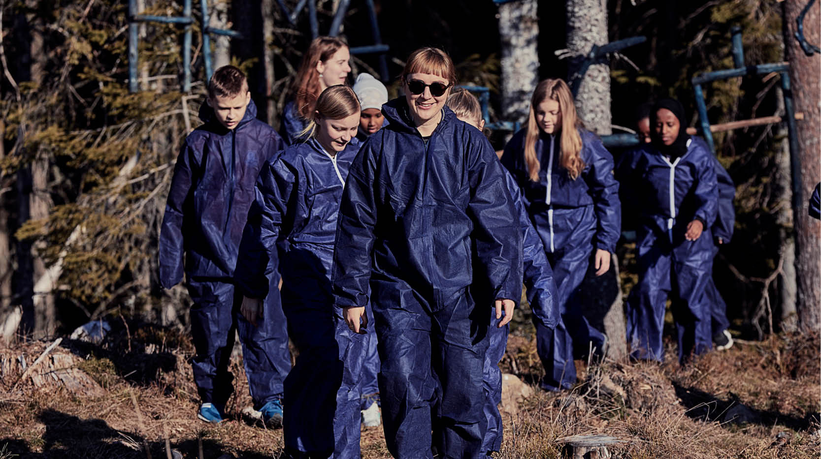 Ungdomar klädda i blå overaller i skogen.