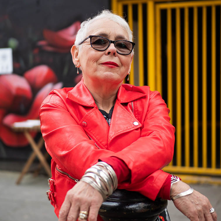 Äldre dam i röd jacka och solglasögon som hänger på en solpe utanför ett café