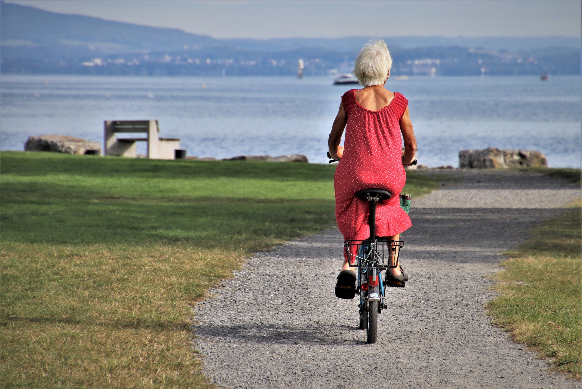 En kvinna i en röd lång klänning som cyklar i ett öppet platt landskap på en grusväg